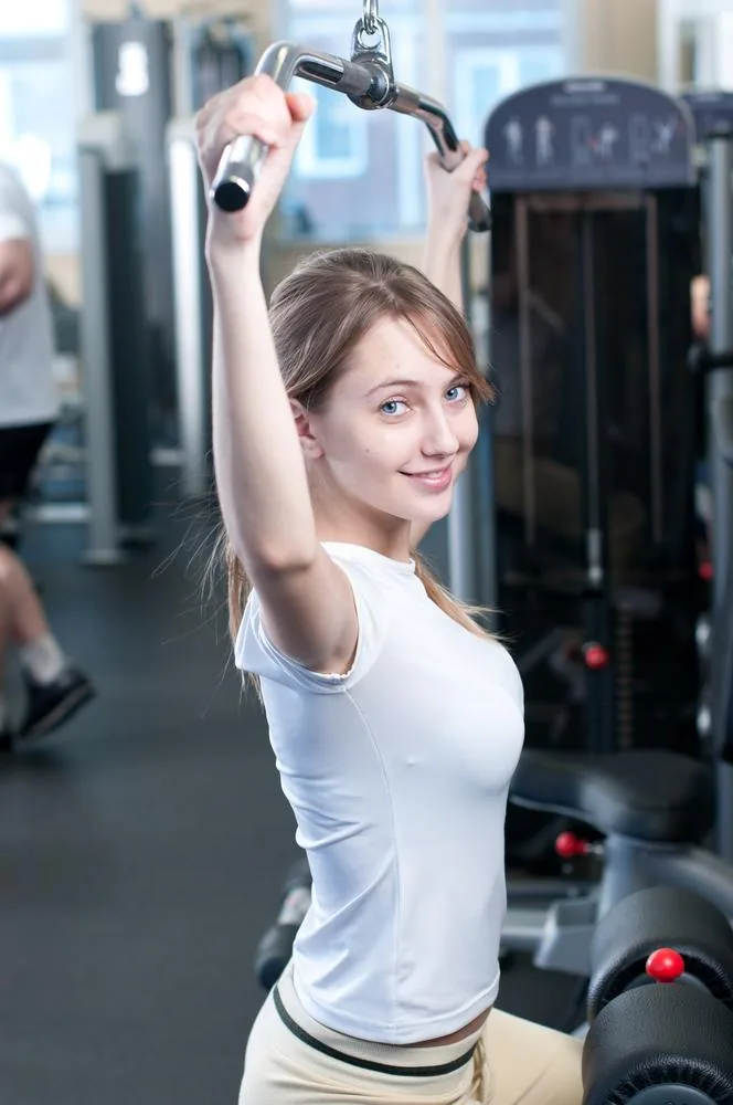 Woman using cable machine for shoulder exercise in gym